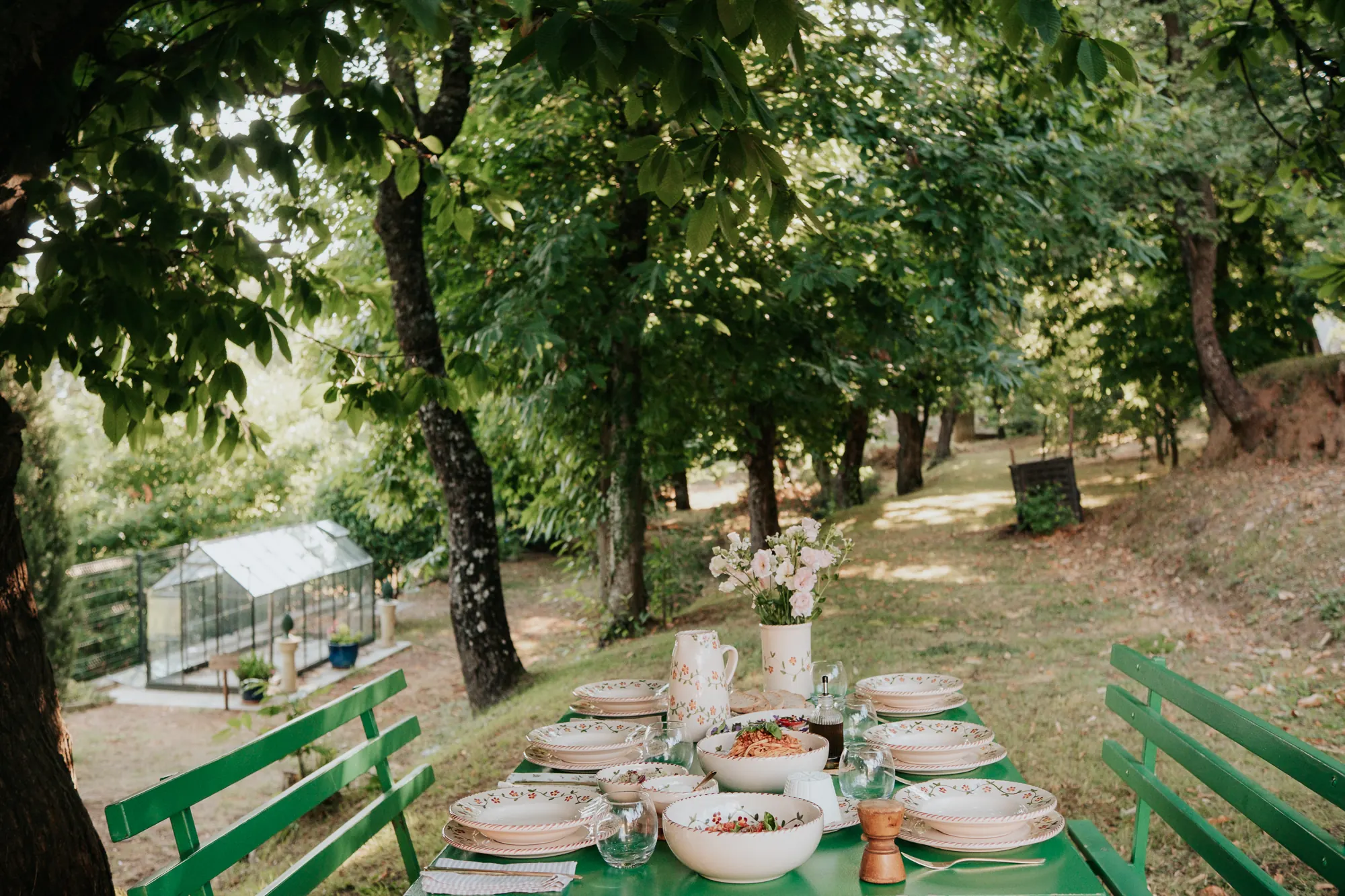 Longue table dressée dans une allée d’arbres au jardin