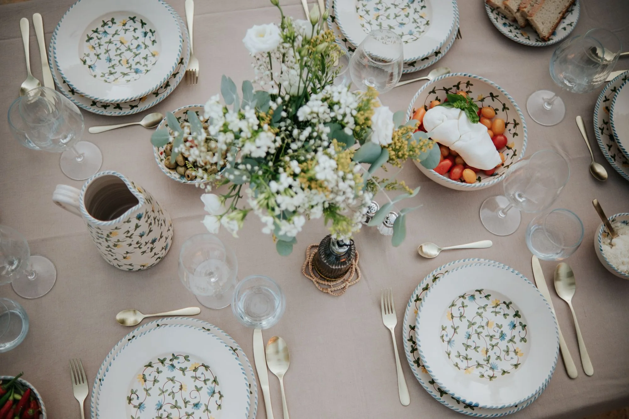 Table dressée vue du dessus avec la vaisselle Fiori di Campo, un bouquet blanc, des olives et une burrata