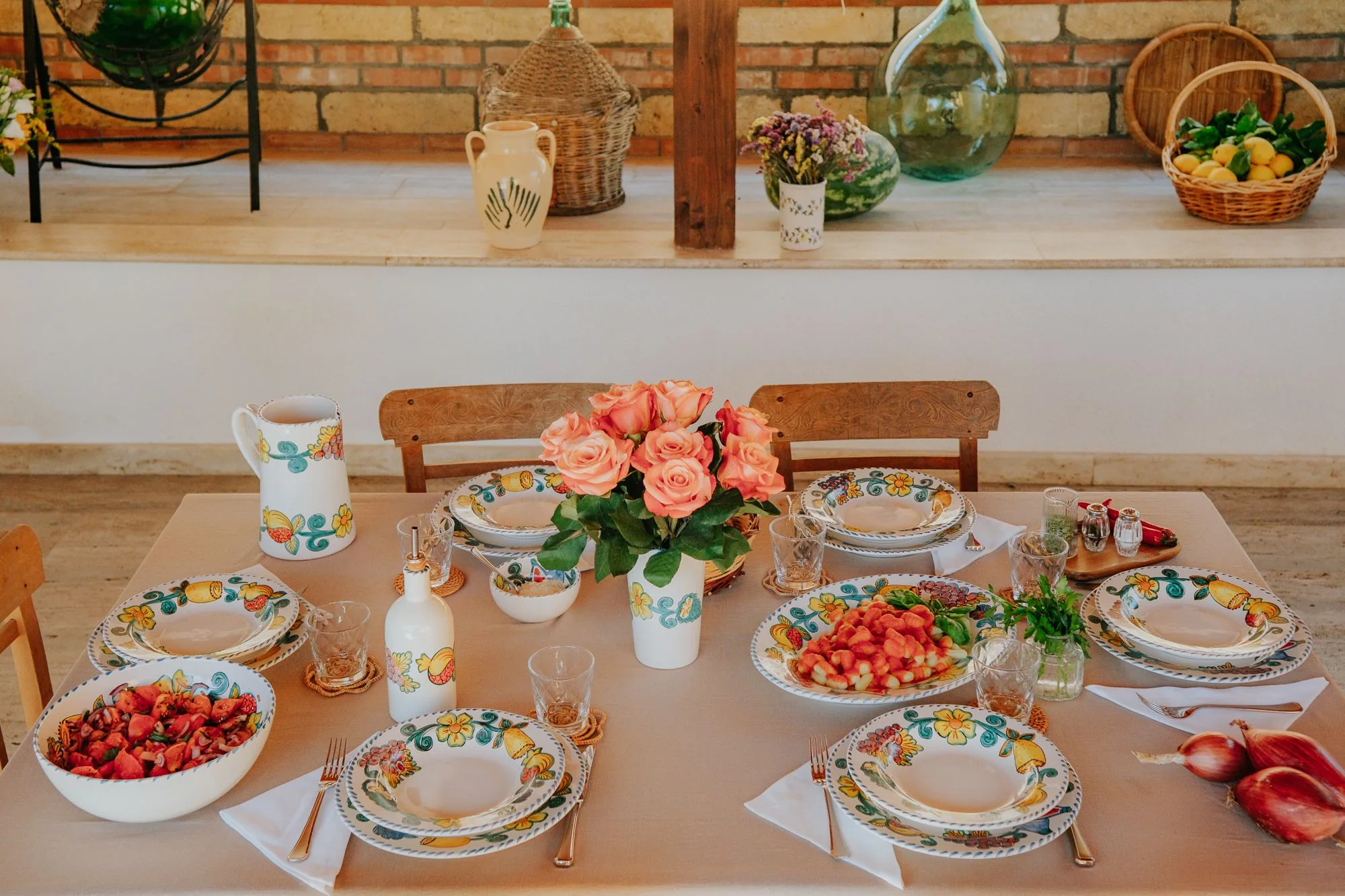 Table dressée pour six avec la vaisselle Frutta del Sud, gnocchis, salade de tomates et roses