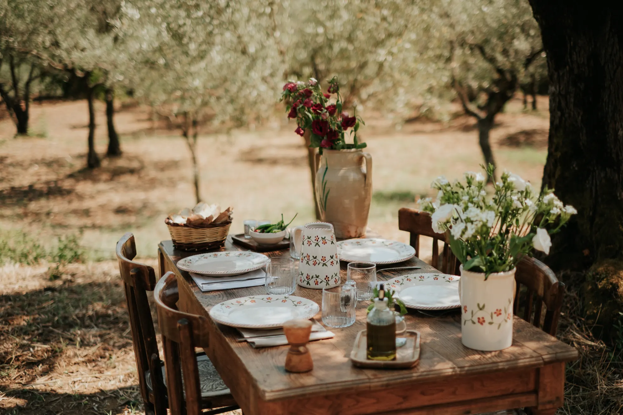 Table dressée dans une oliveraie avec bouquets et carafes