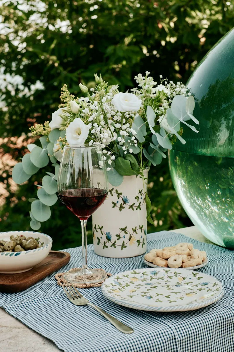 Verre de vin rouge, bouquet blanc et vaisselle Fiori di Campo sur une nappe